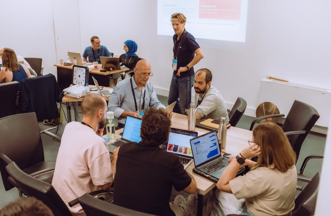 A group of participants collaborating around a table covered in laptops